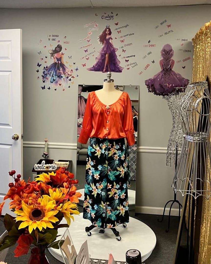 The atelier: an orange satin blouse and floral trousers on a dress form, with sunflowers on the counter