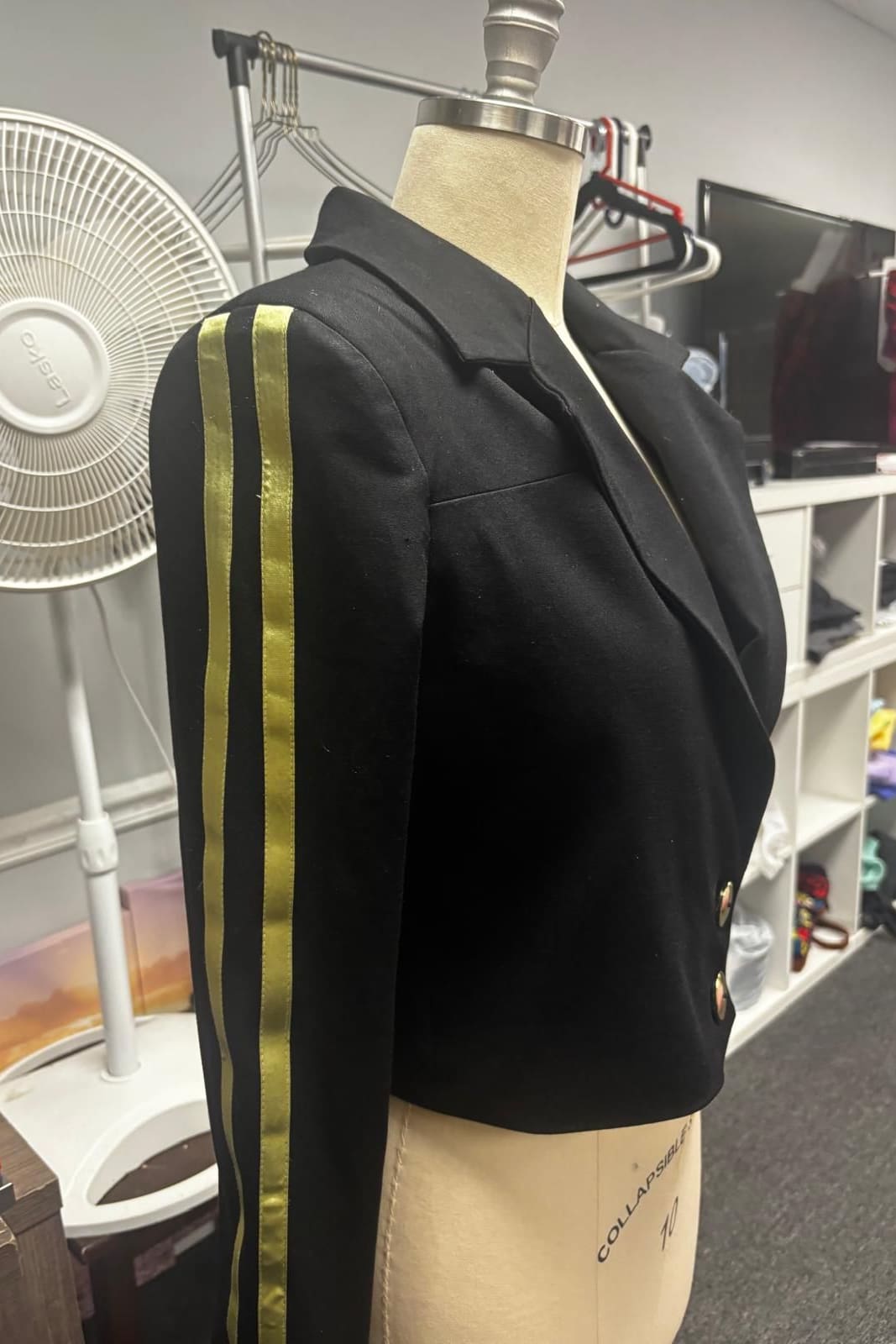 Cropped black blazer with two gold stripes down the sleeve on a dress form