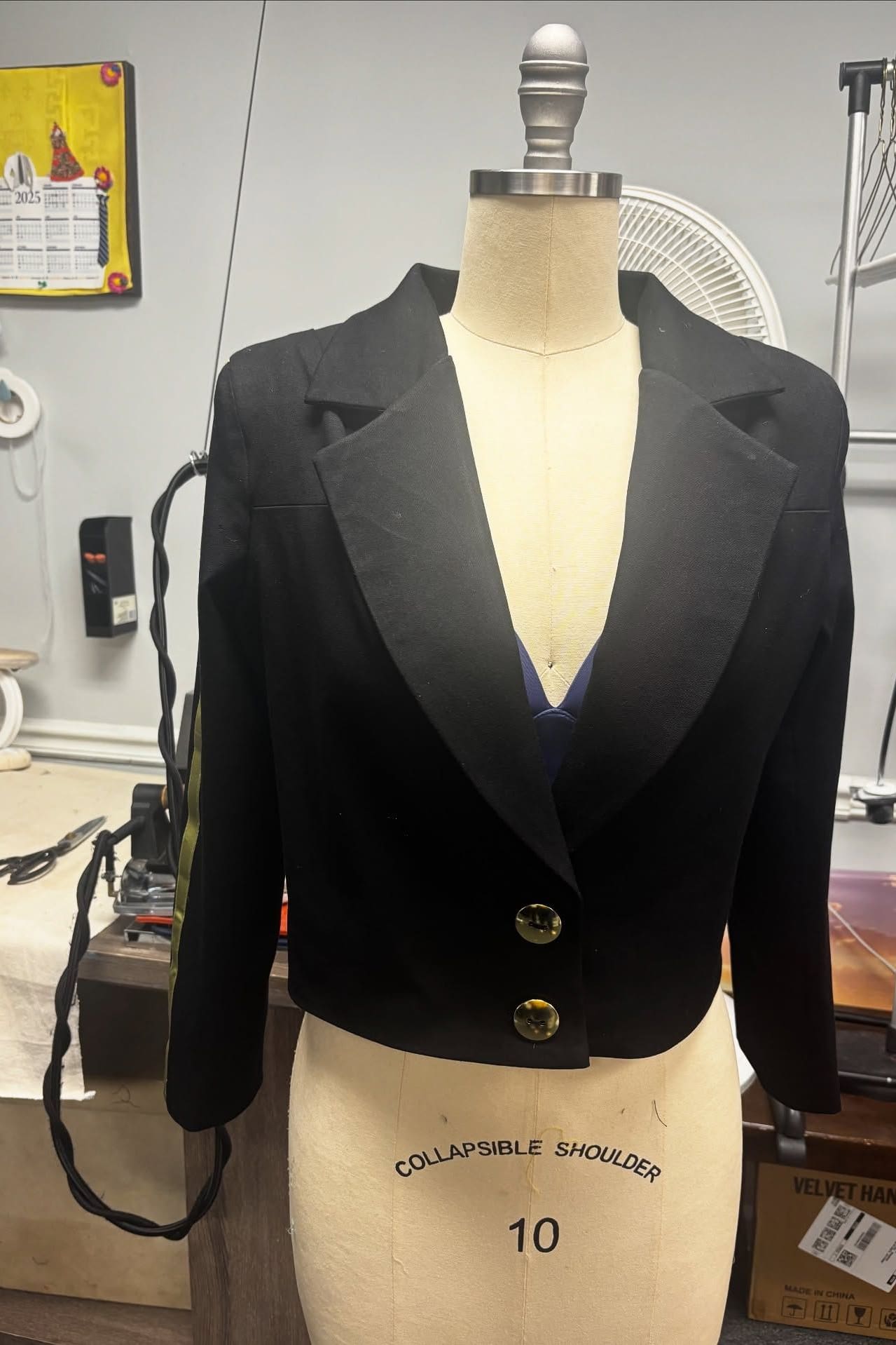 Tailored black cropped jacket with gold buttons on a dress form