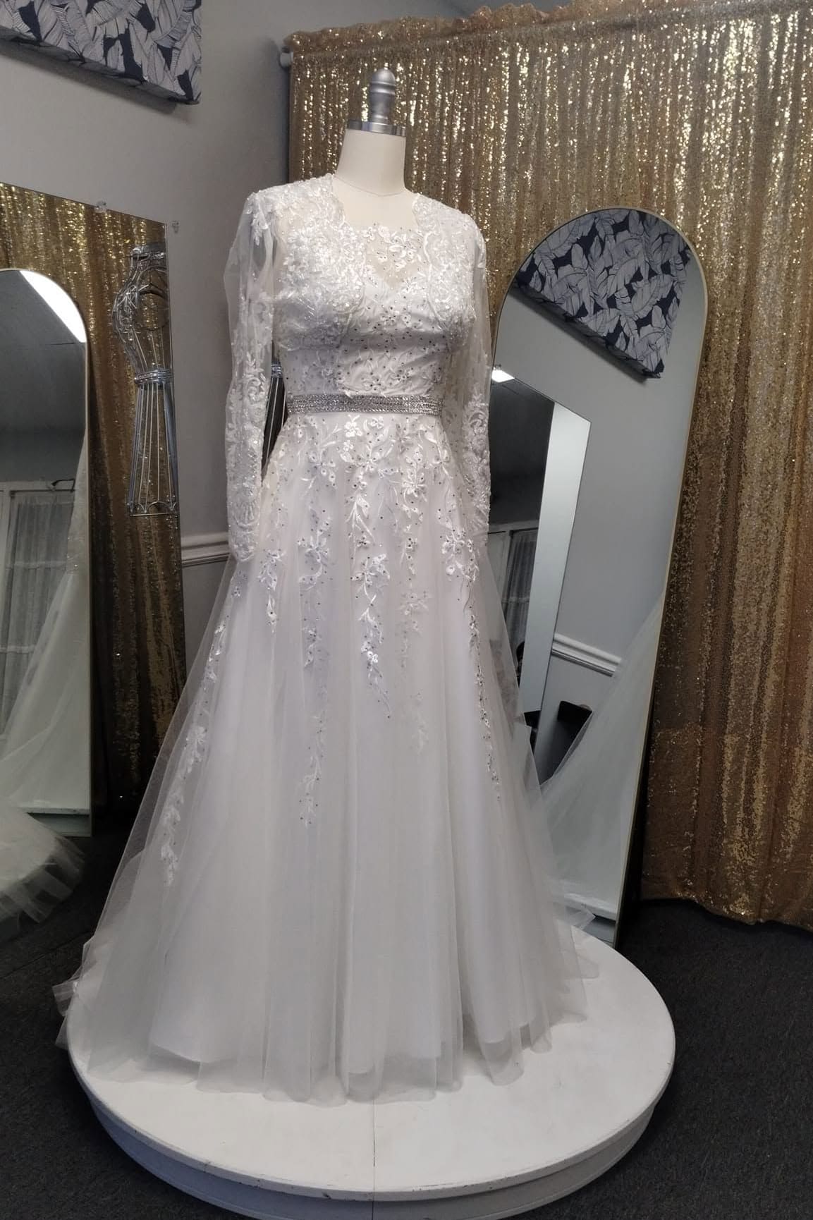 Long-sleeve lace wedding dress with a tulle skirt on a showroom turntable