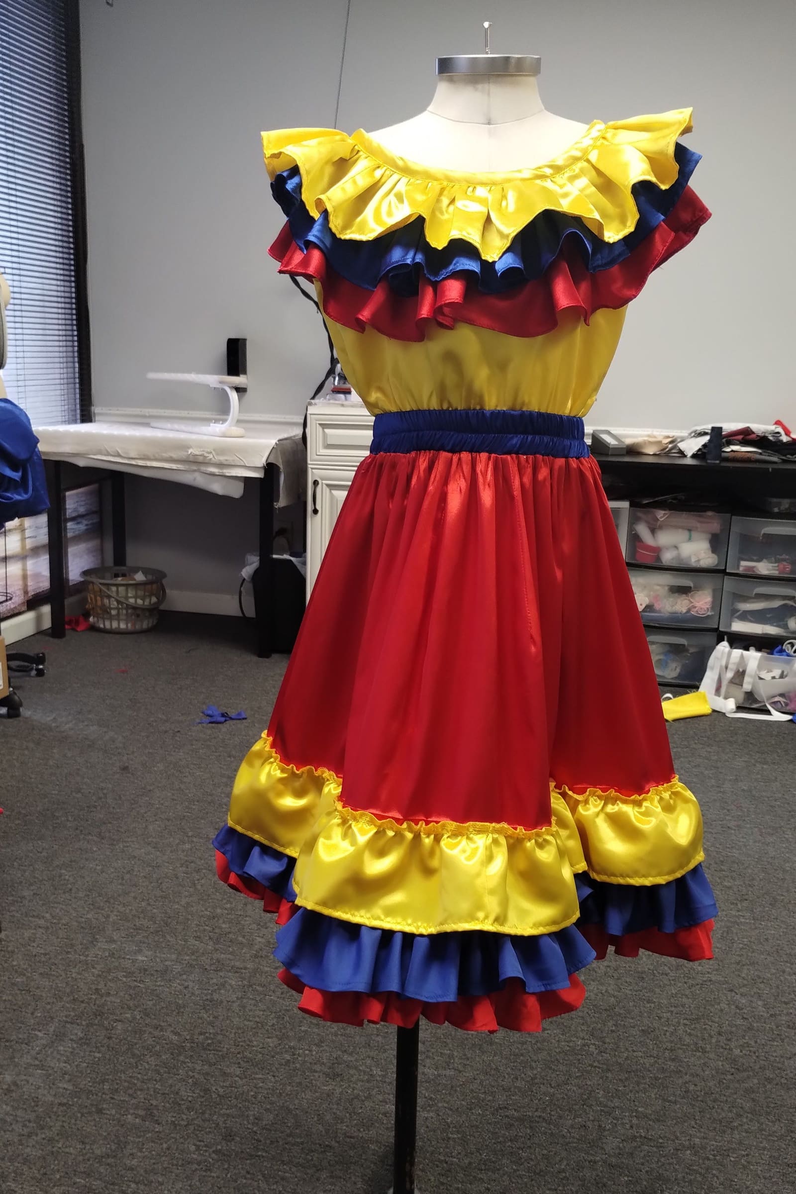 Traditional Colombian folkloric dress with yellow, blue and red ruffles on a stand