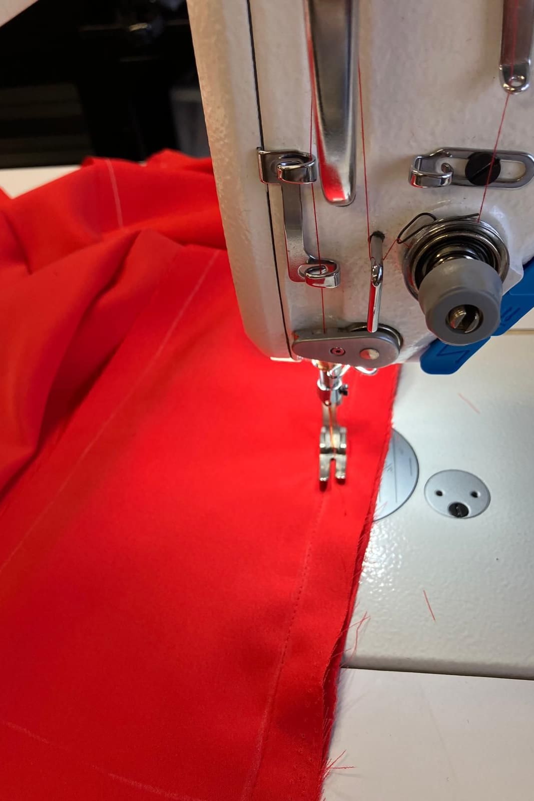 A sewing machine needle stitching a seam in red crepe