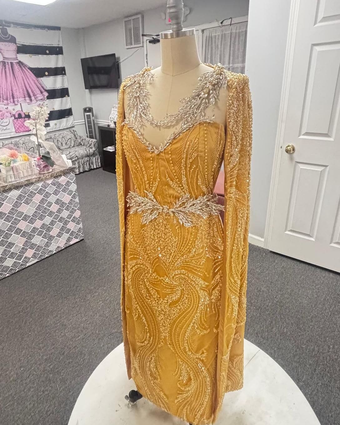 Gold beaded column gown with a silver-embroidered neckline and matching cape on the fitting platform