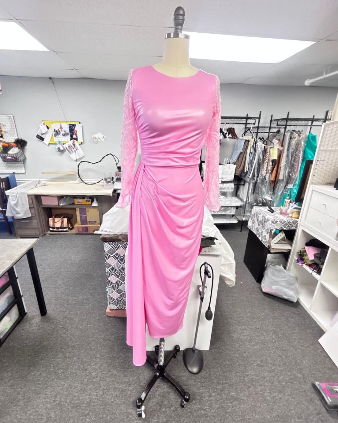 Fitted pink dress with long lace sleeves and a draped skirt on a dress form in the workroom