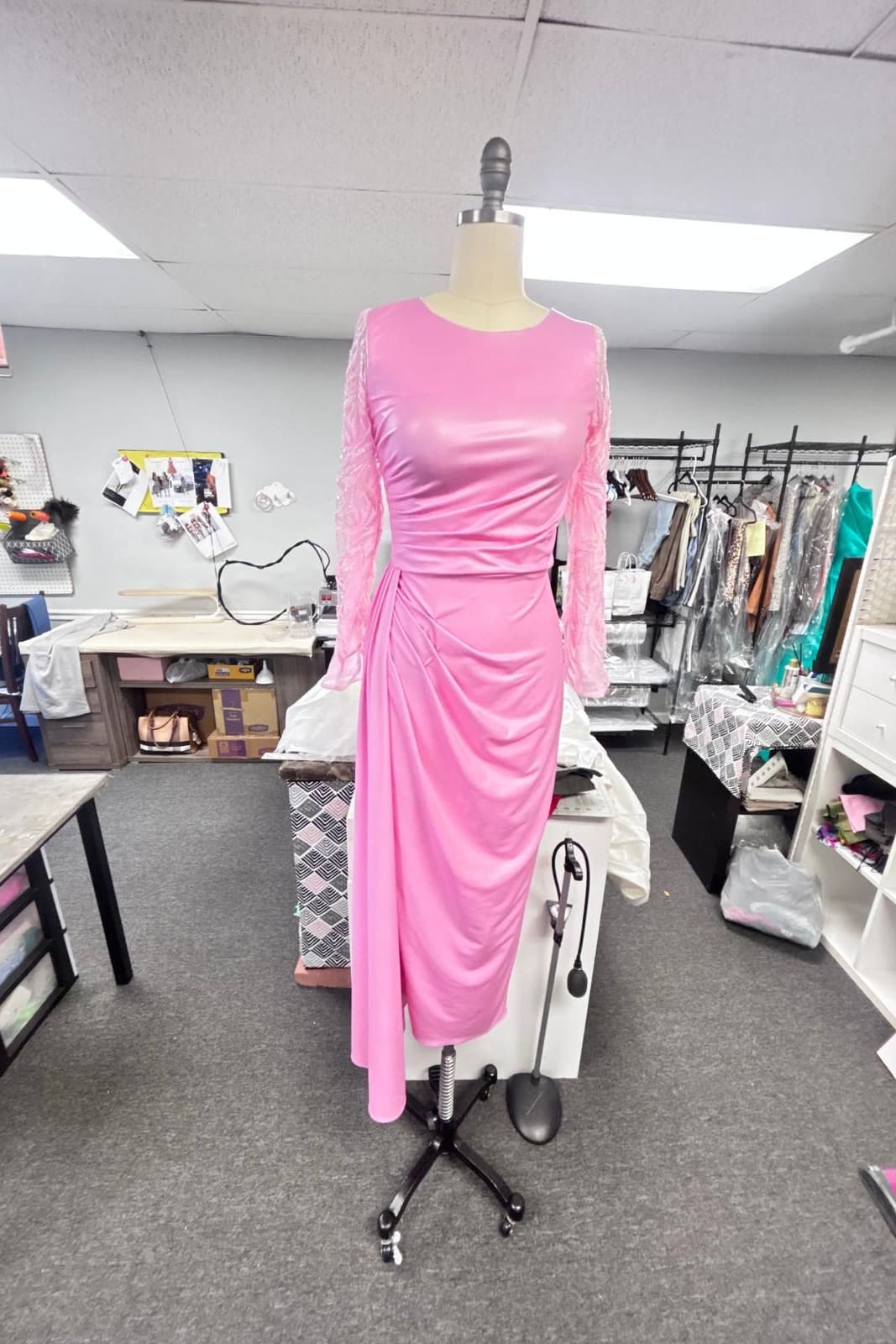 Fitted pink dress with long sleeves and a gathered drape at the hip on a dress form