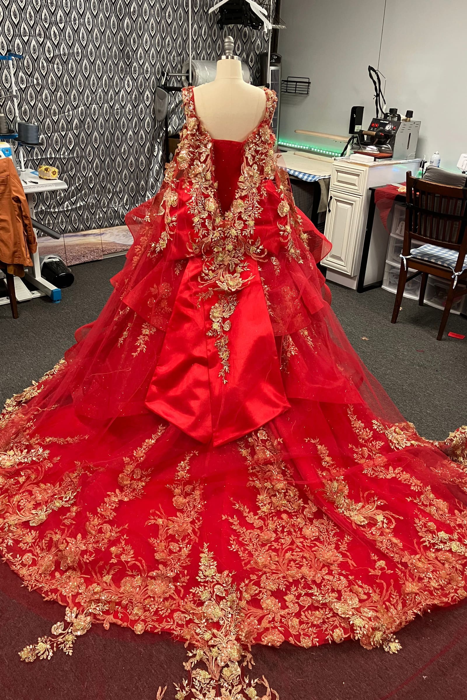 Back of a red ball gown with gold lace appliqués, a large bow and a cathedral train