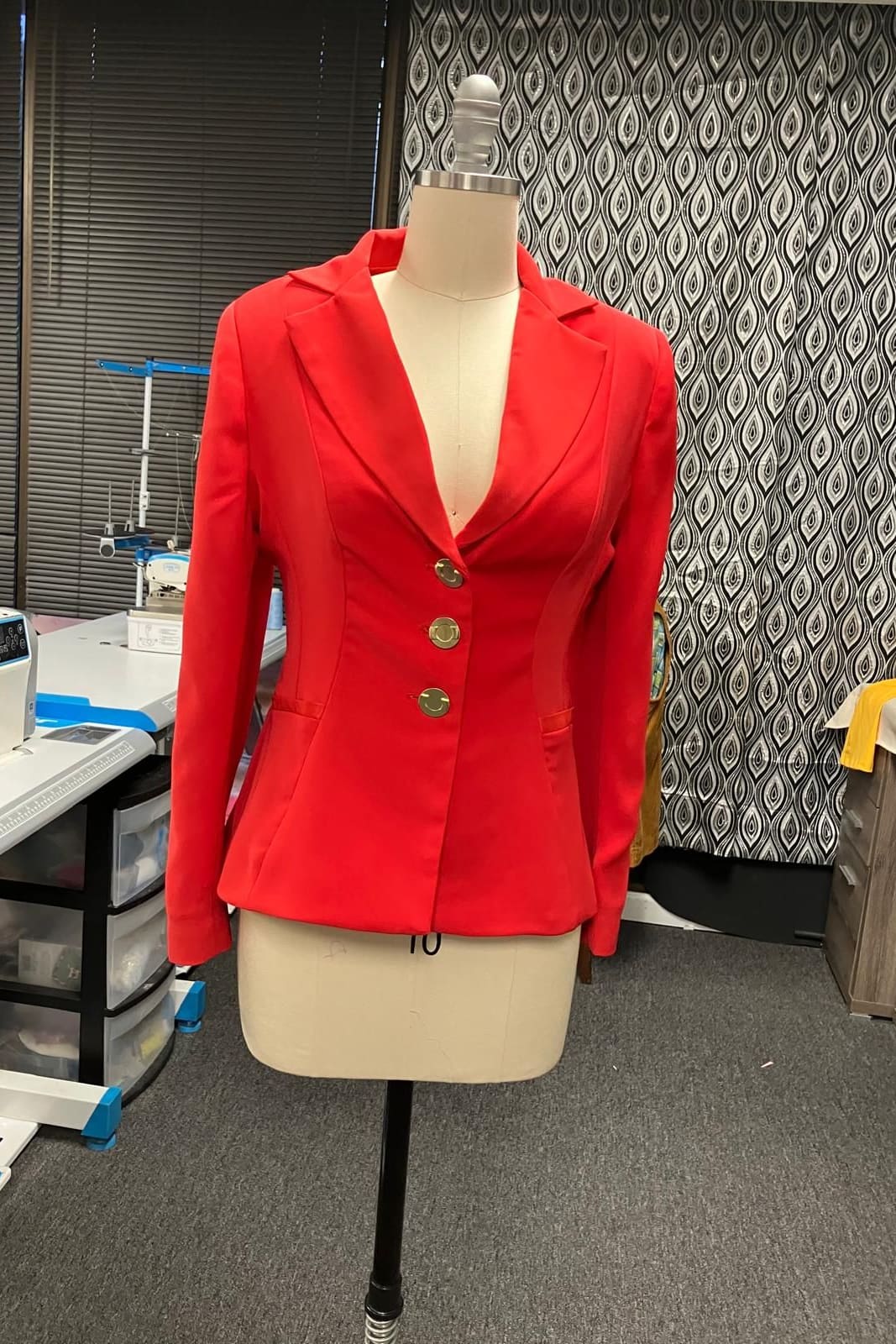 Fitted red blazer with gold buttons on a dress form